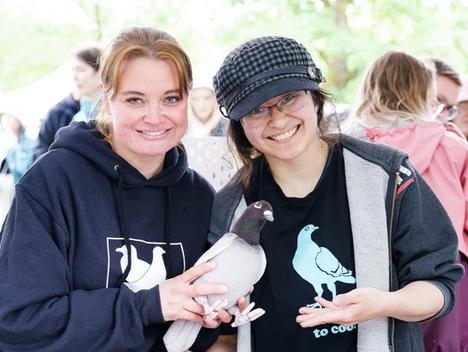 To kvinner smiler i kamera, den ene holder en duebamse i hendene, den endre later som om hun holder en fugl, men fuglen er et trykk på T-skjorten hennes. 