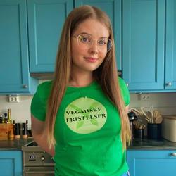 Bilde av Tiril Holseter på kjøkkenet i grønn T-skjorte med teksten "Veganske Fristelser"