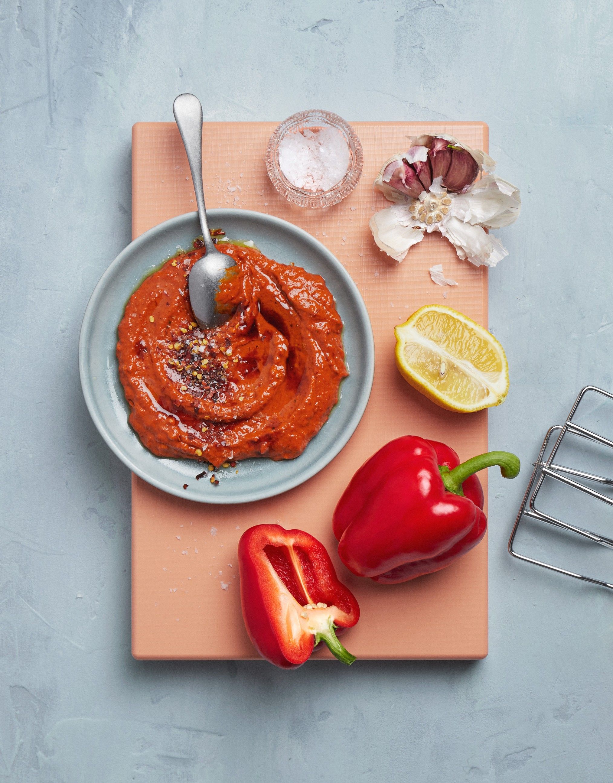 Muhammara i en skål på en skjærefjøl, med paprike og sitron ved siden av