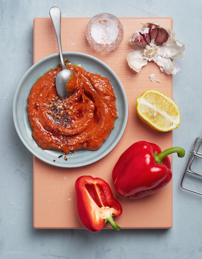Muhammara i en skål på en skjærefjøl, med paprike og sitron ved siden av