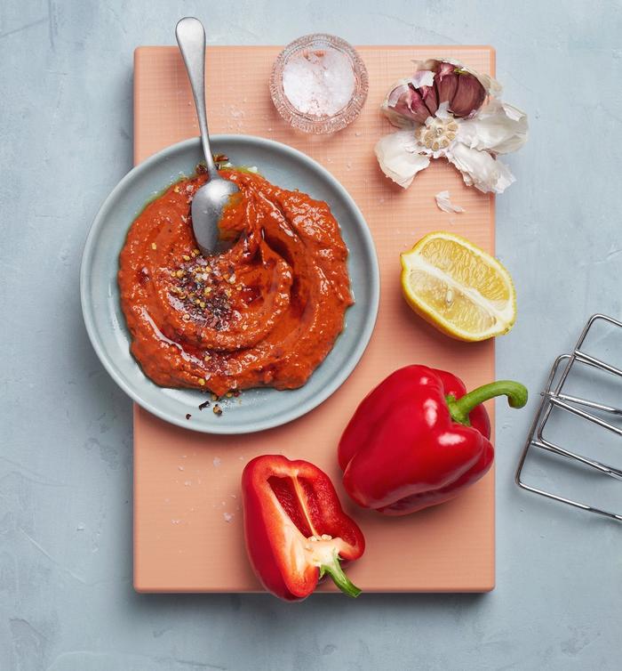 Muhammara i en skål på en skjærefjøl, med paprike og sitron ved siden av
