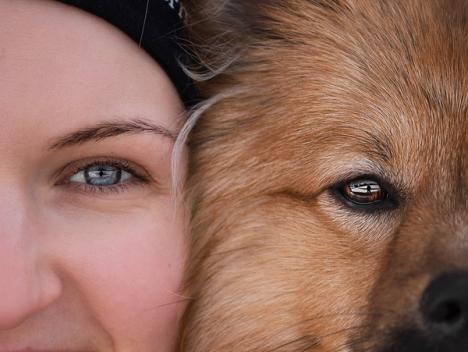 Et bilde av en kvinne og en hund som ser i kamera, zoomet tett inn på ansiktene deres så bare halve ansiktet er synlig
