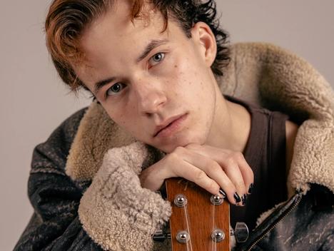 Ung mann med kort hår som lener seg på gitar