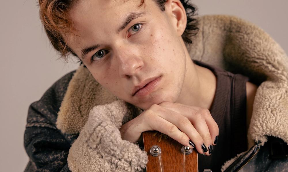 Ung mann med kort hår som lener seg på gitar