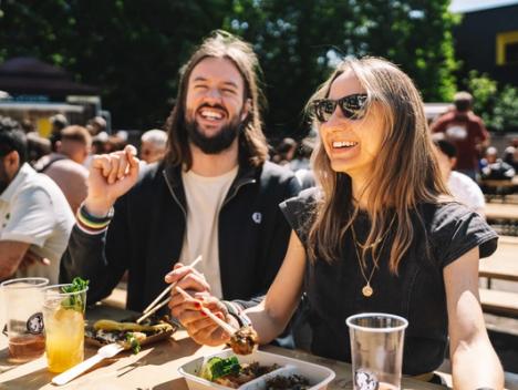 En kvinne og en mann koser seg med god mat i sollyset mens de smiler