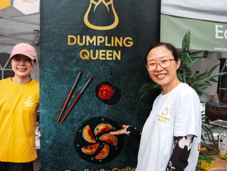 Bilde av en dumpling som blir holdt av to spisespinner og har blitt dyppet i soyasaus