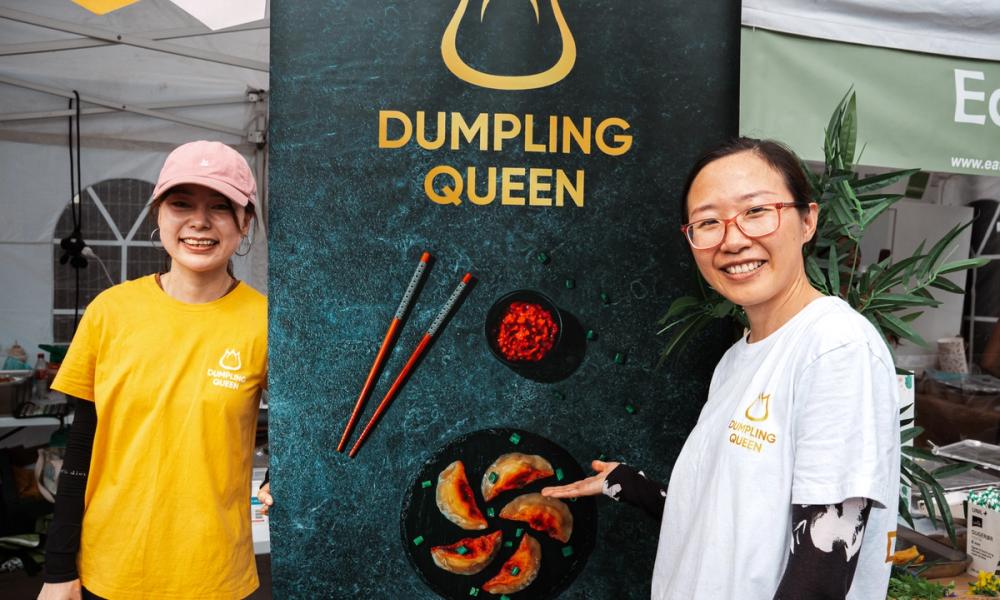 Bilde av en dumpling som blir holdt av to spisespinner og har blitt dyppet i soyasaus