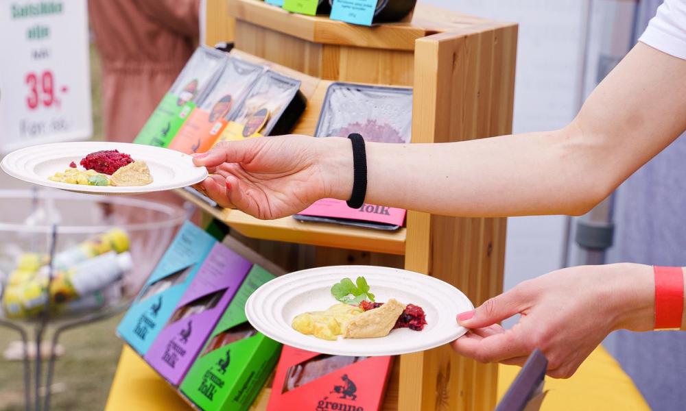 Bilde av hender som deler ut gratis smaksprøver på Grønne Folks produkter.