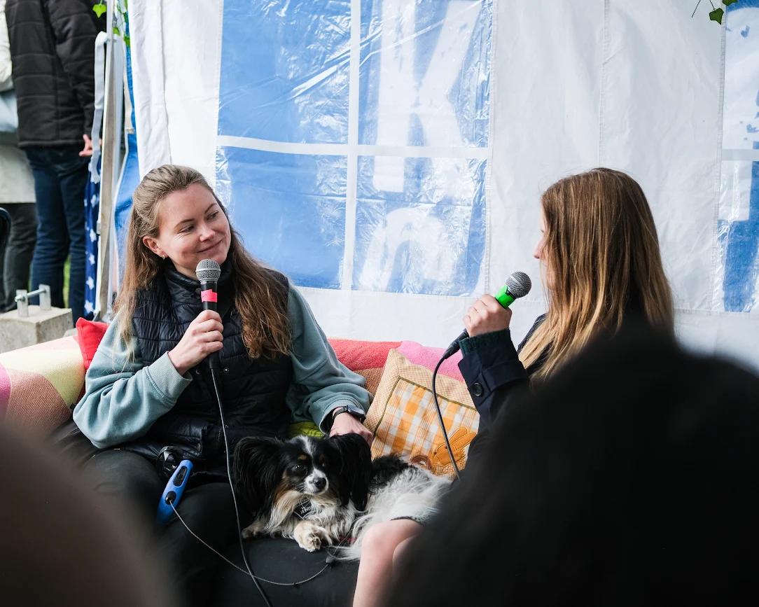 To kvinner sitter i en sofa og prater. En hund ligger mellom dem. 