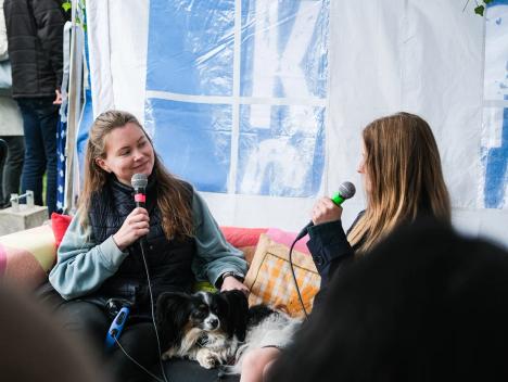 To kvinner sitter i en sofa og prater. En hund ligger mellom dem.