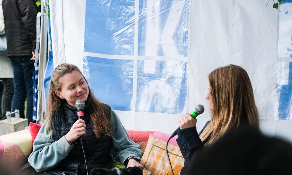 To kvinner sitter i en sofa og prater. En hund ligger mellom dem.