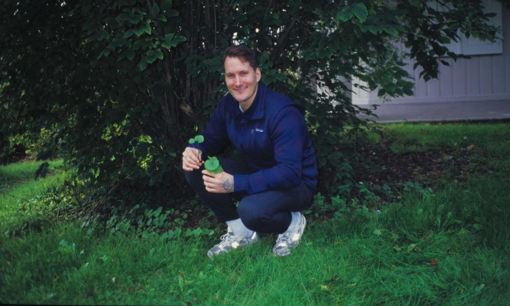 Mann sitter på huk under et tre