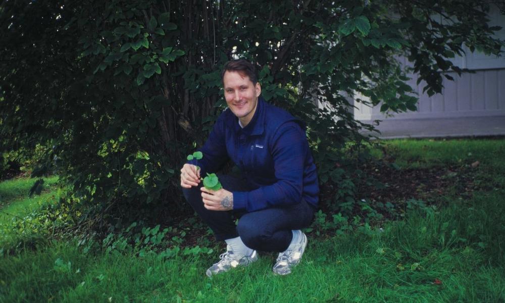 Mann sitter på huk under et tre