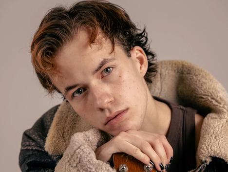 Ung mann med kort hår som lener seg på gitar
