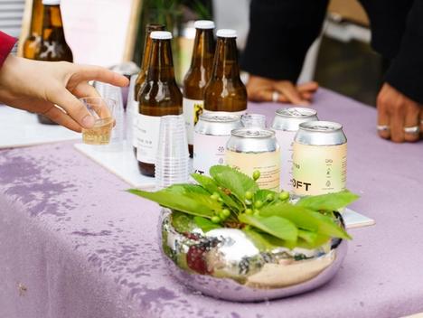 Bilde av en hånd som får en smaksprøve på drikken Villbrygg, med flasker og bokser med Villbrygg synlige i bildet. 