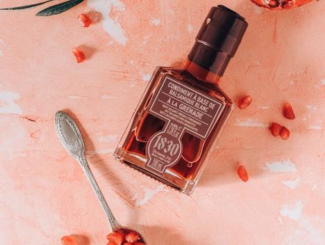 Bilde av flaske med granateple-balsamico, oppskåret granateple, og skje med granateplefrø