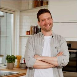 Bilde av Kristoffer på kjøkkenet med grønnsaker i forgrunnen og en gryte.