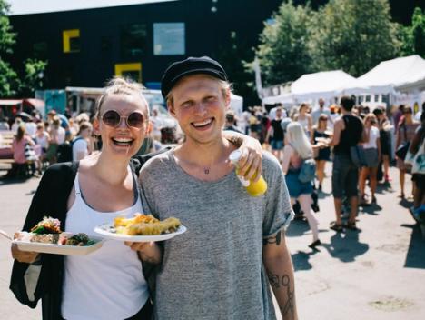 En kvinne og en mann ser i kamera, smiler og holder hver sin tallerken med mat.