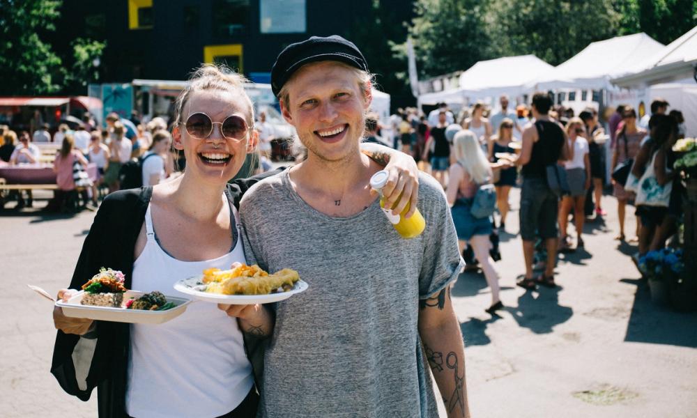 En kvinne og en mann ser i kamera, smiler og holder hver sin tallerken med mat.