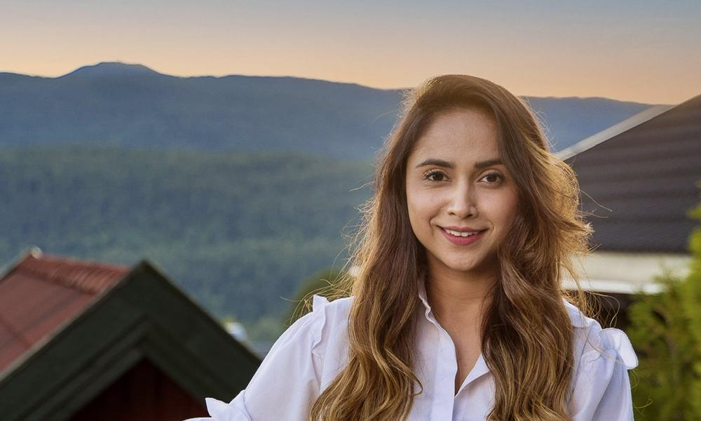 Sakirat Waraich holder en kurv med grønnsaker med norsk landskap i bakgrunnen.