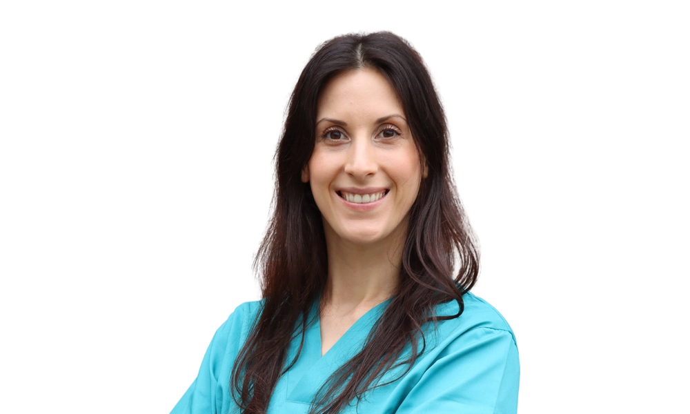 Smilende bilde av Claire Lucie Sonck med langt brunt hår og armer i kors, iført turkis veterinæruniform.