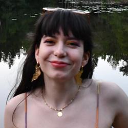 Kvinne med solbriller på hodet som smiler foran en innsjø