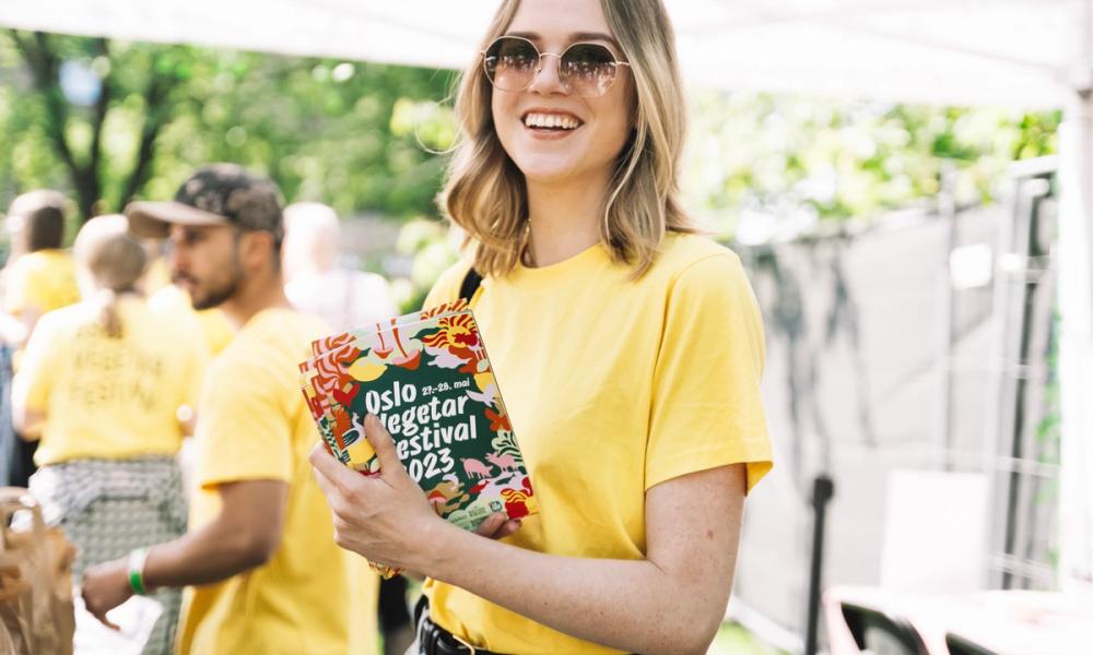 Frivillig i gul skjorte som holder en bunke med flyers fra fjorårets festival