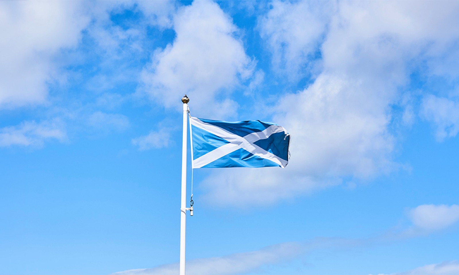 Scottish saltire flag flying against a blue sky with white clouds