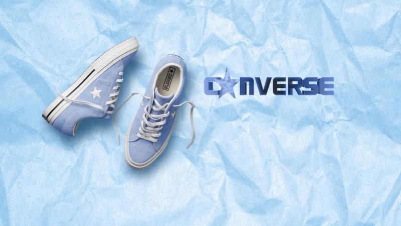 3D letters settling into text reading "Converse" with the paper star as the "O". Pair of blue converse low tops to the left of logo. Light blue, paper background. 