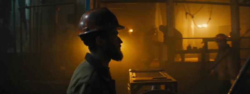 Midshot of miner walking through underground workshop, with other miners in background.