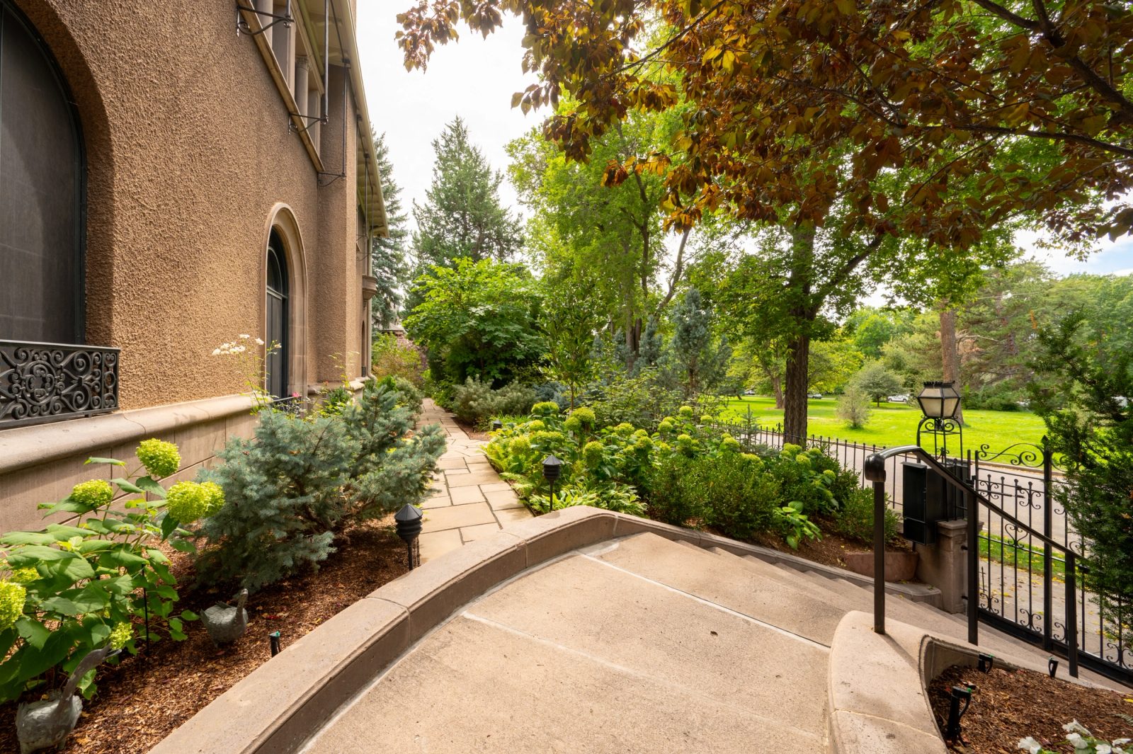 A curved walkway descends past planting beds to an iron gate and lawn.