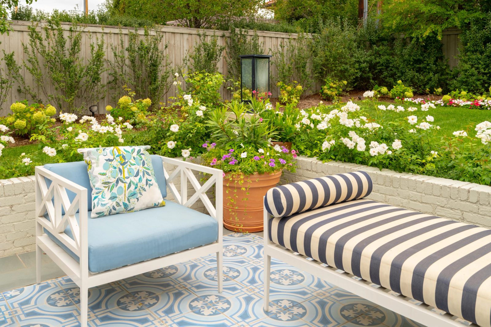 Blue lounge chair and striped daybed beside blooming beds.