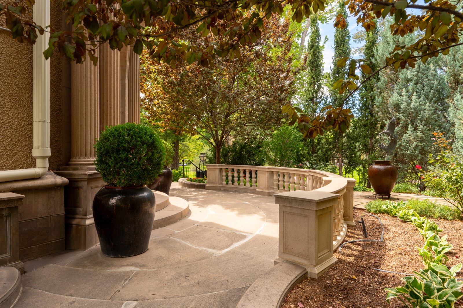 A stone terrace corner with a potted boxwood topiary beside classical columns.