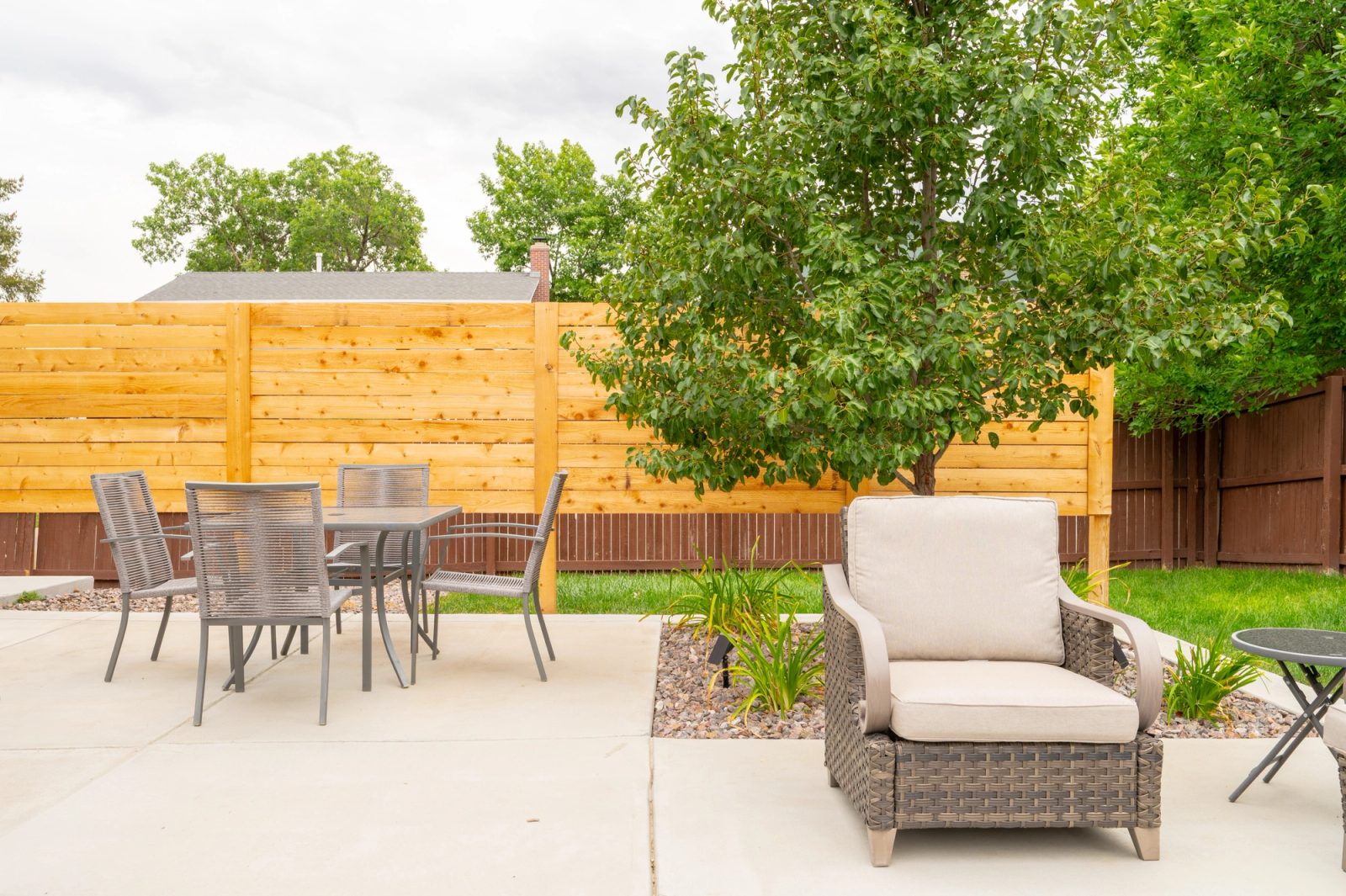 Outdoor dining set and lounge chair on a concrete patio in front of a horizontal cedar privacy screen.