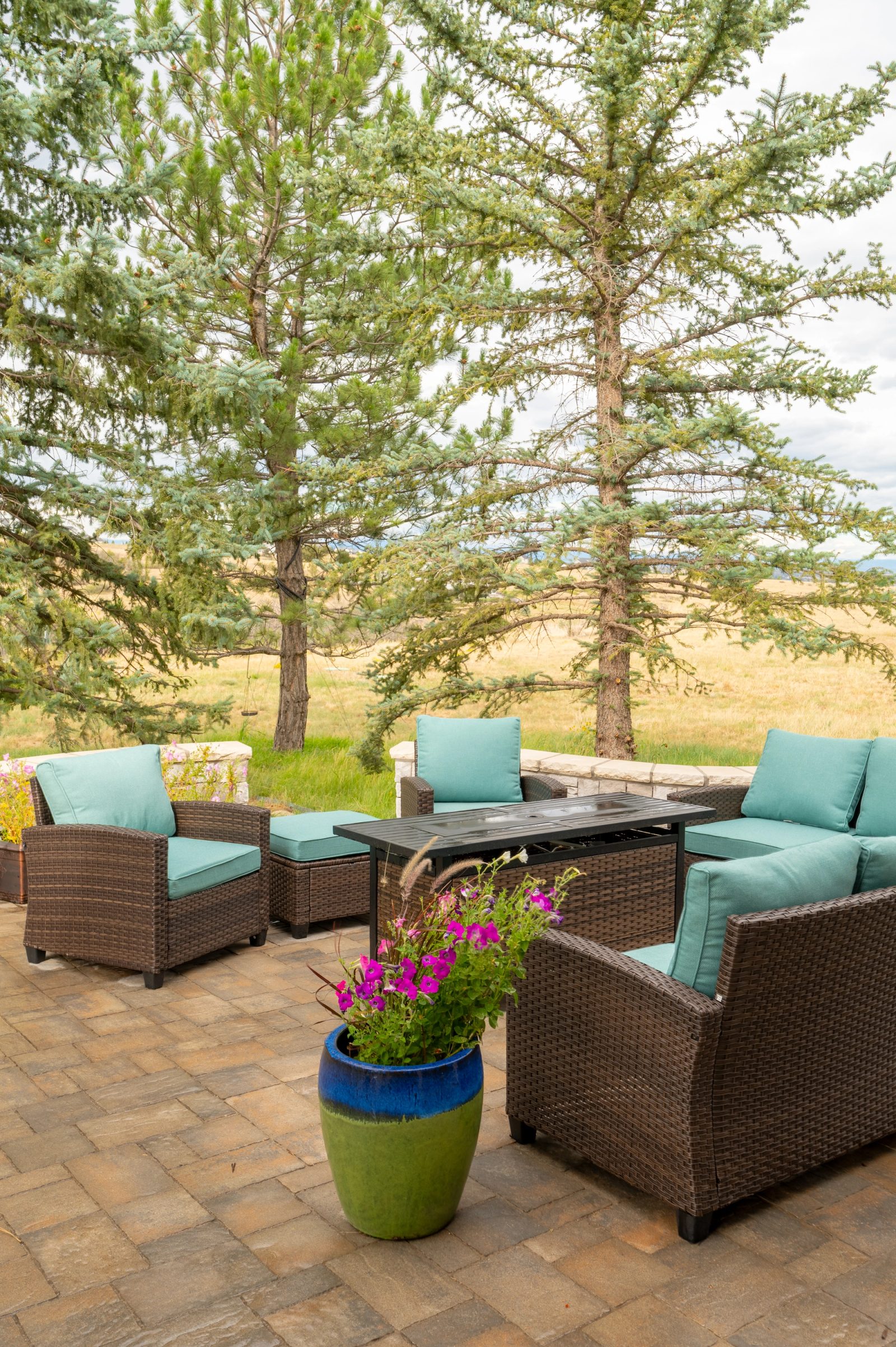 Vertical view of patio seating with a flowering planter under tall pines.
