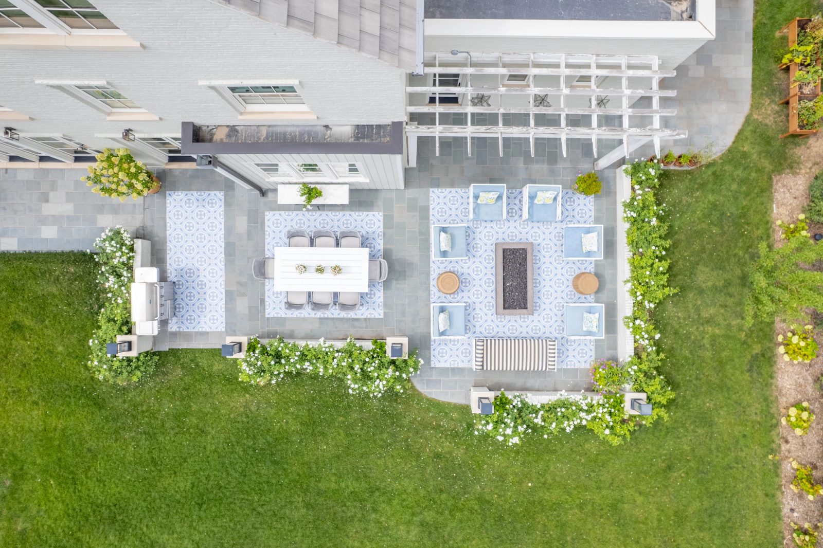 Linear fire pit centered among blue lounge chairs under a white pergola.