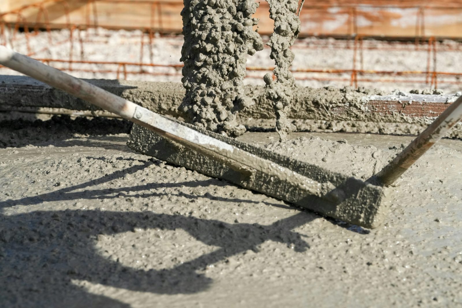 Fresh concrete pouring from a chute while a screed board levels the wet slab surface.