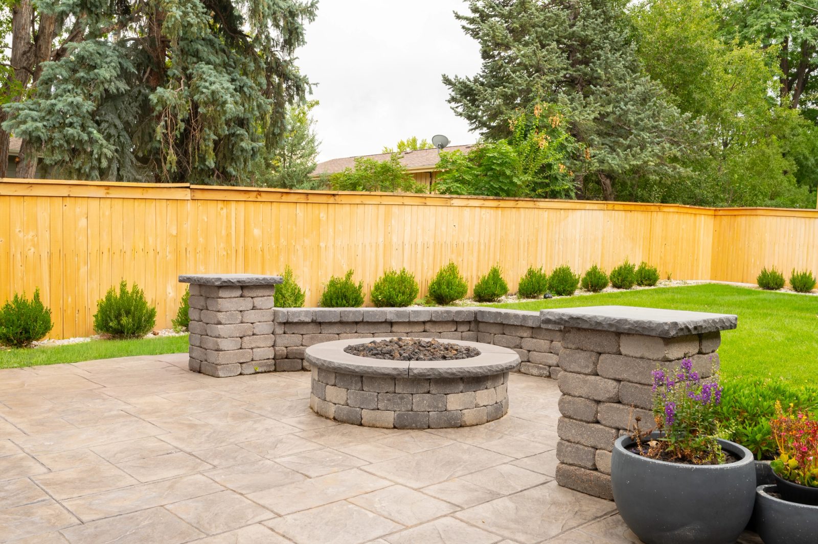 Stamped concrete patio leading to a stone fire pit enclosure along a cedar fence.