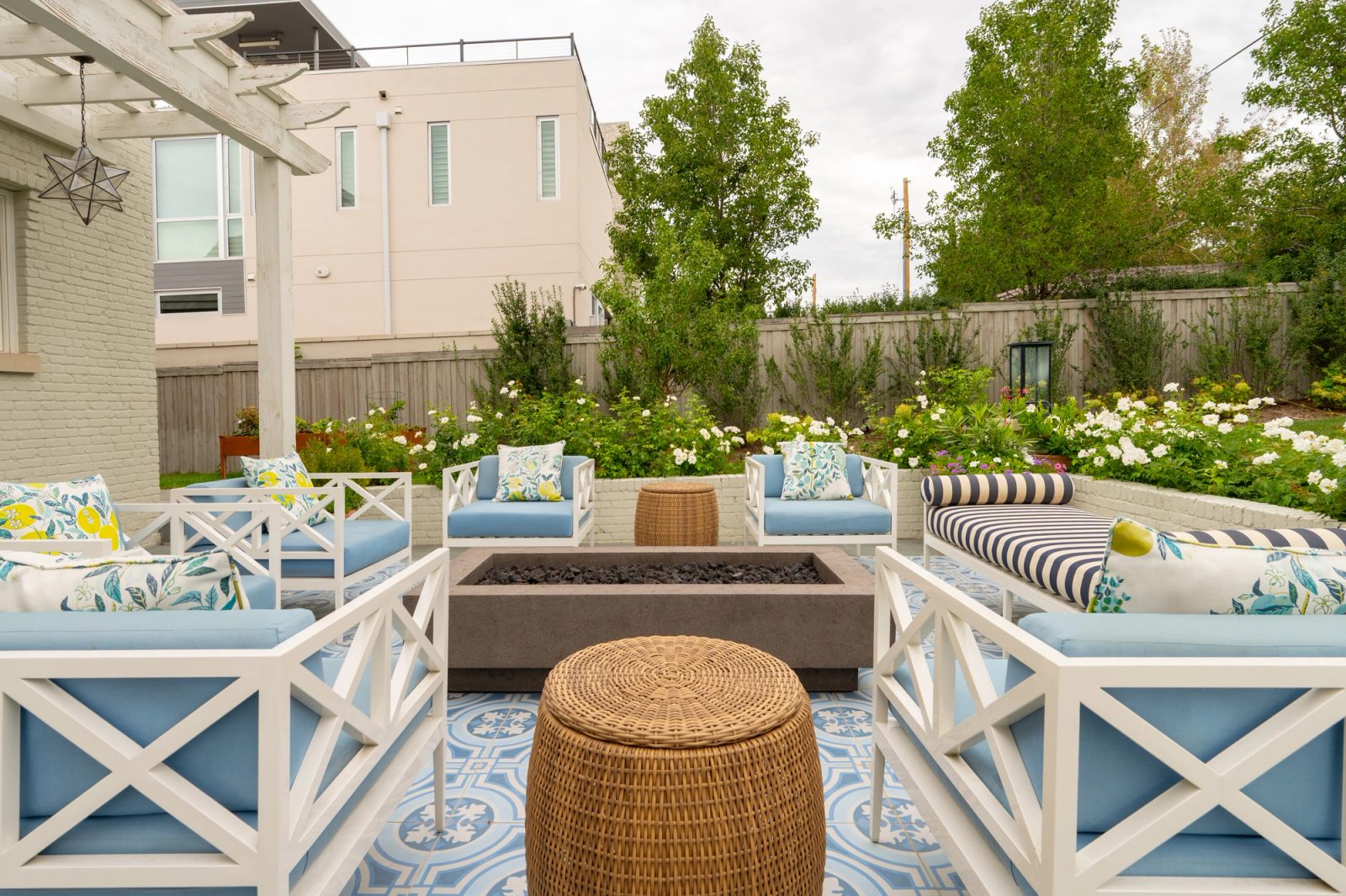 Wicker ottoman and white chairs around a fire pit on patterned tile.