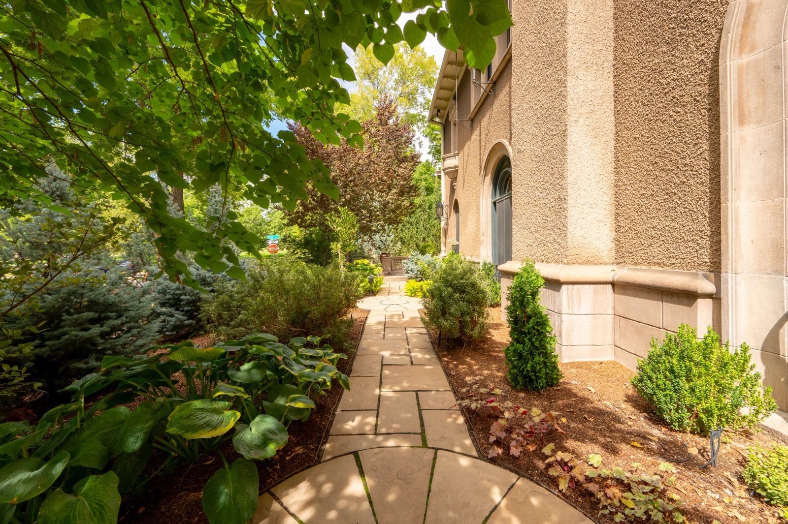 Flagstone path winding through a shaded hosta and shrub garden beside the house.