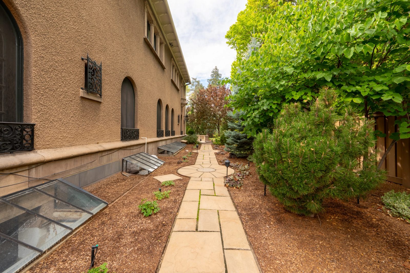 A narrow flagstone path runs between garden beds and the house wall.