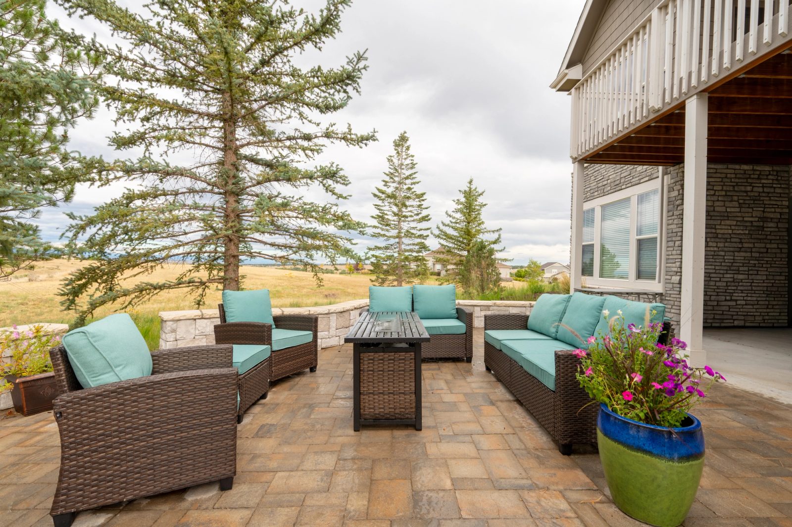 Paver patio seating area with a fire table and bright flower planter beside the house.