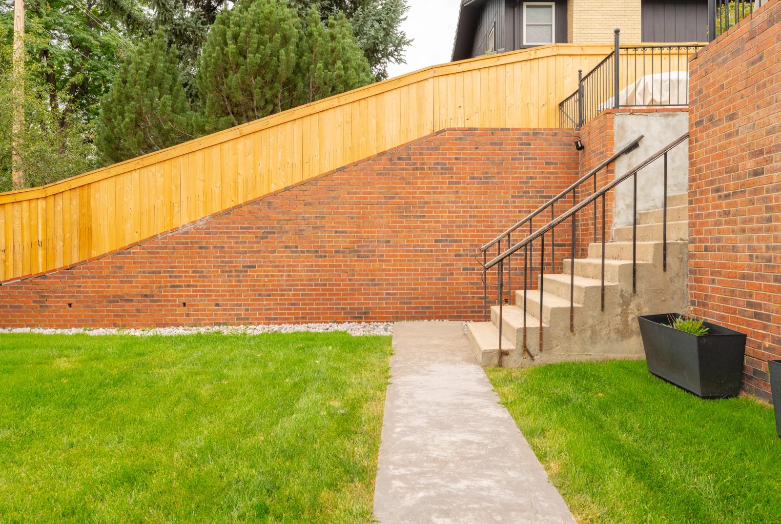 Concrete path leading to steps beside a brick retaining wall and a stepped cedar fence.