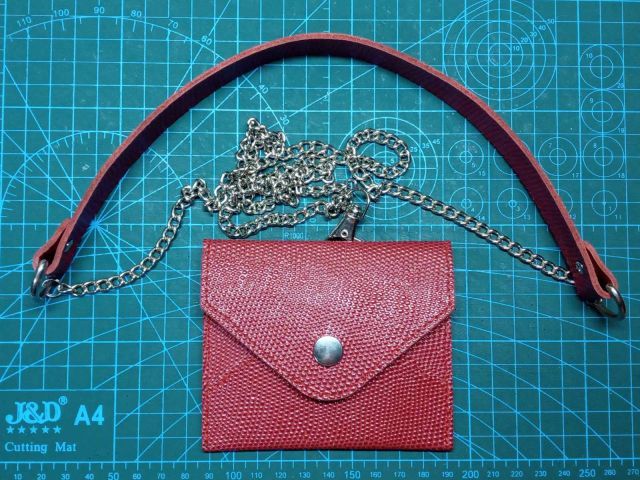 Mini borsa rossa in pelle stile busta con tracolla e catena metallica su tappetino da taglio