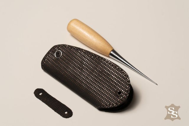 Porta-chiavi scuro in pelle testurizzata con bottone, fatto a mano, vicino a strumento da pelletteria