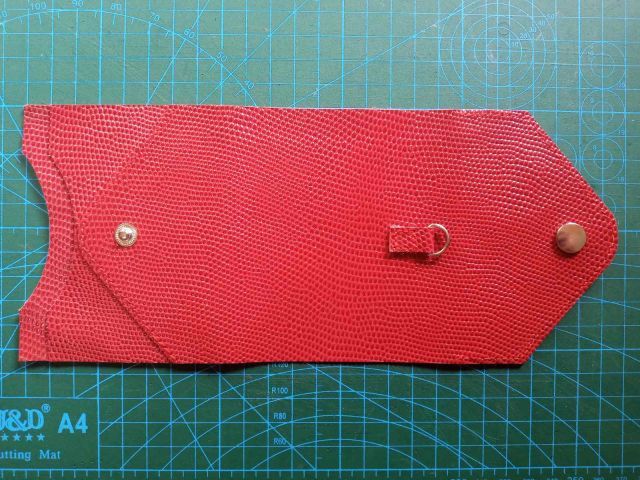 Червона шкіряна міні-сумка конверт із ремінцем та металевим ланцюжком на фоні розкрійного килимка