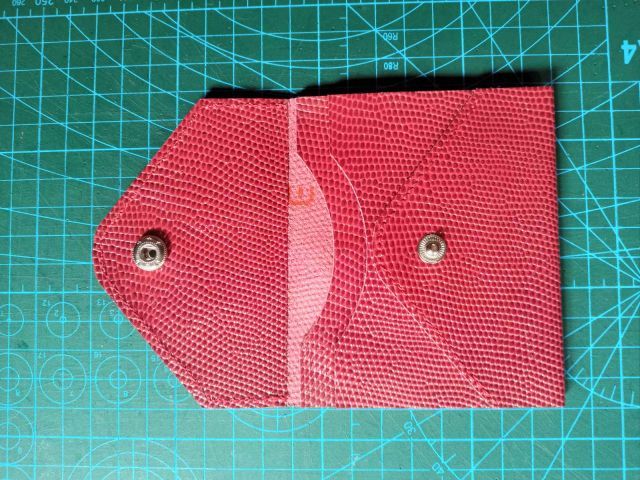 Червона шкіряна міні-сумка конверт із ремінцем та металевим ланцюжком на фоні розкрійного килимка