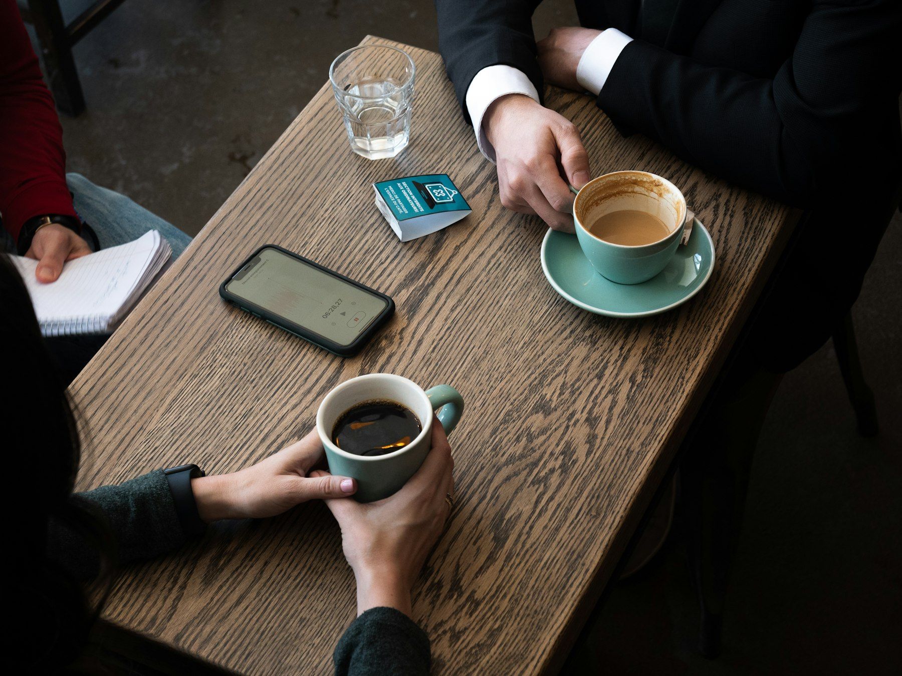 Two people across a wooden table, coffee between them, mid-interview