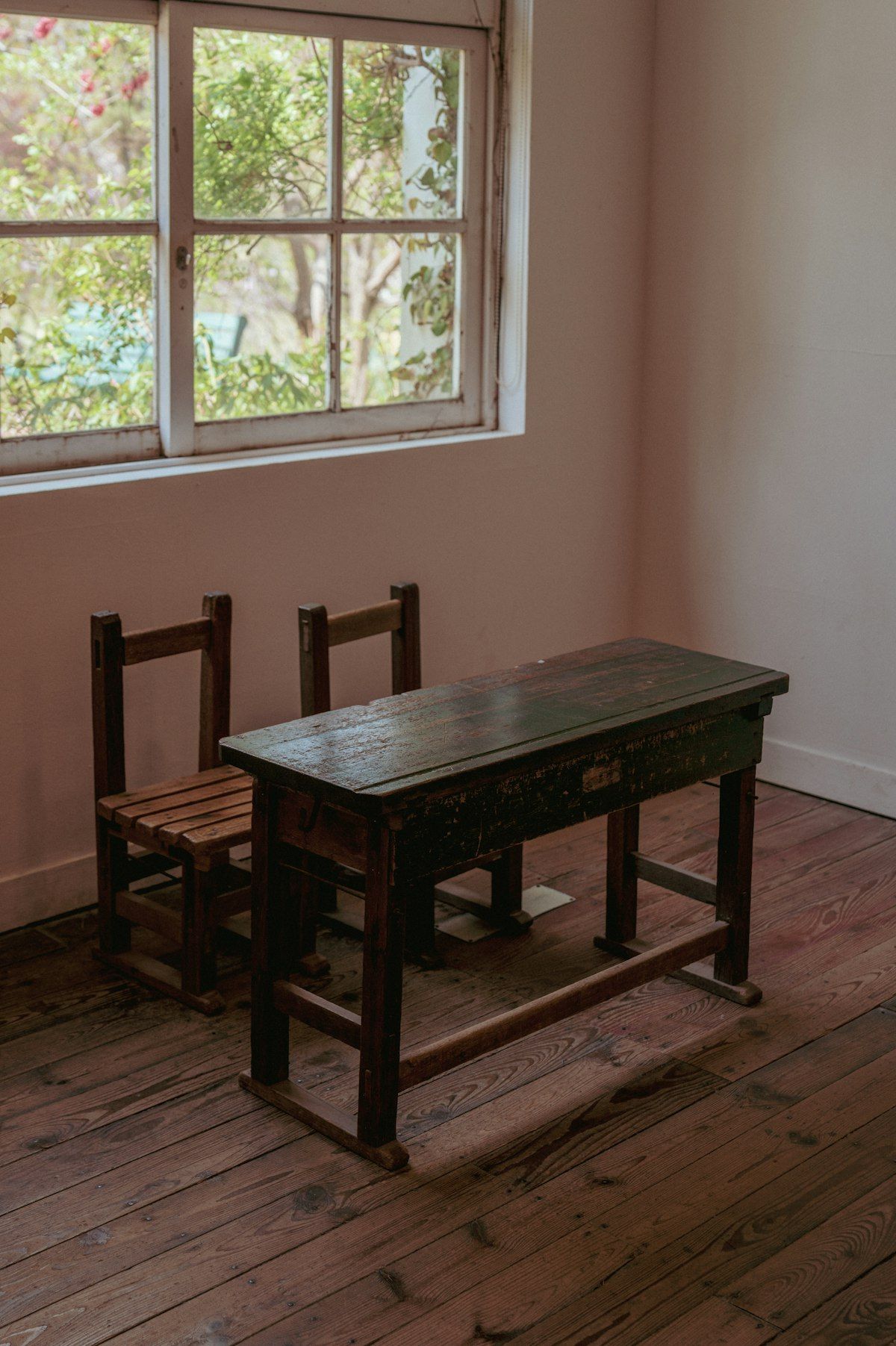 An old desk and two empty chairs by a window