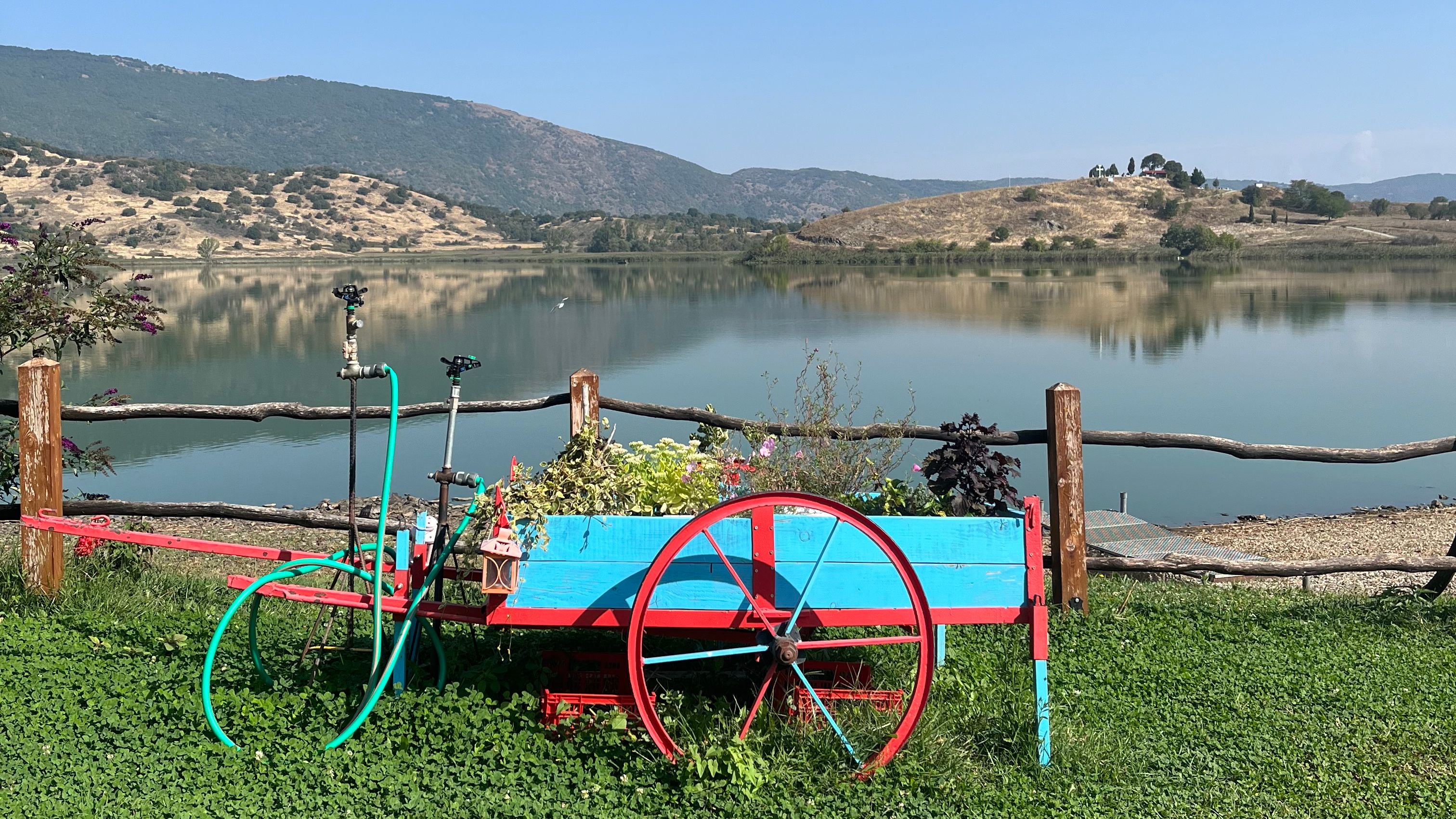 Picture of a lake and mountains in the background with a cyan and red repurposed cart as a gardening pot in the front.d
